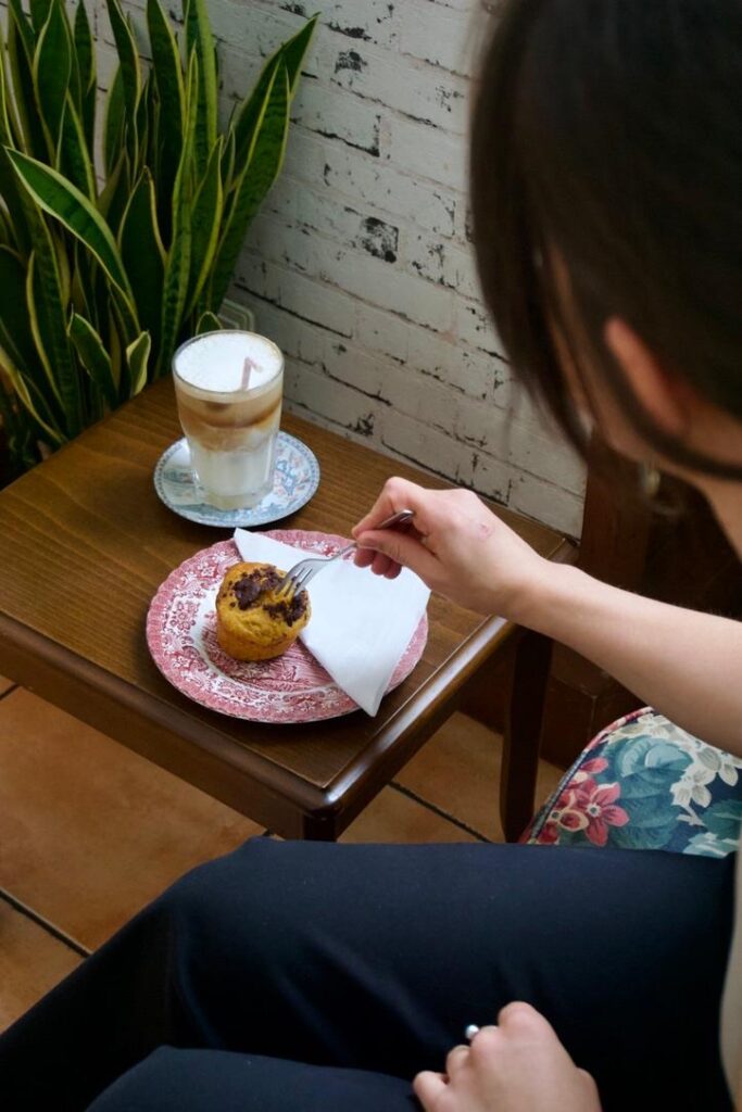 Frau isst Muffin und trinkt Milchkaffee